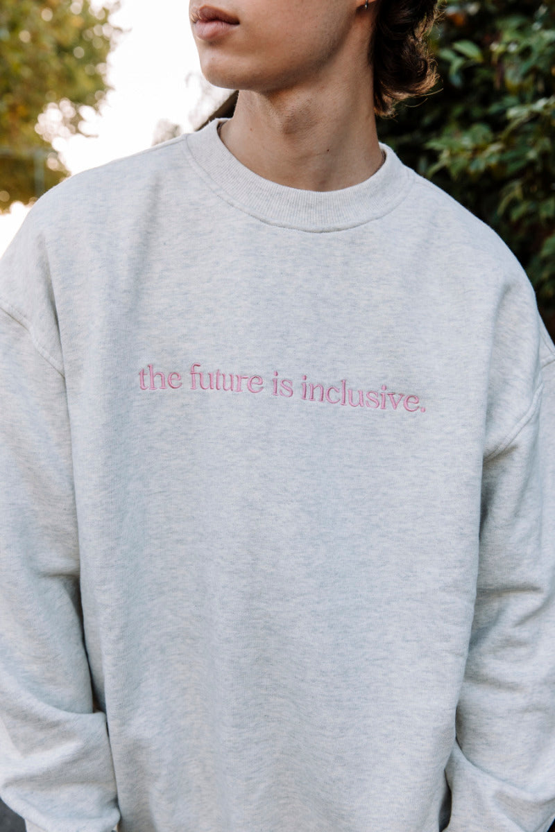 Person wearing a gray sweatshirt with 'the future is inclusive' text embroidered on it.