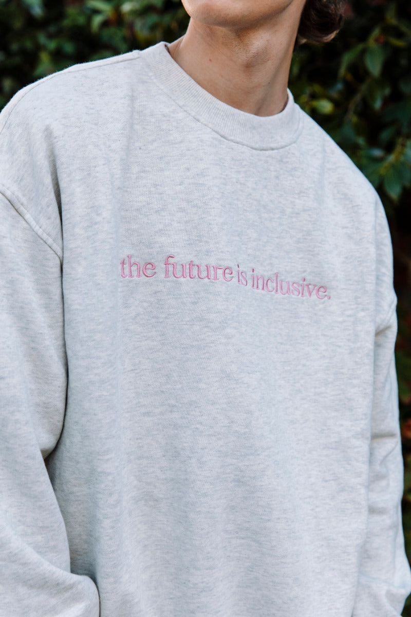Person wearing a light grey marle sweatshirt with 'the future is inclusive' text.