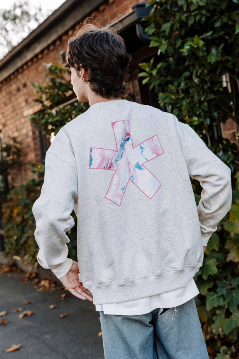 Person wearing a light grey marle sweatshirt with a colorful asterisk logo on the back, standing outdoors.