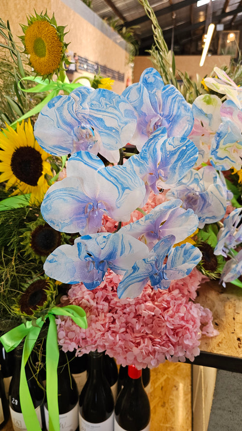 Bouquet of flowers with blue and pink flowers, sunflowers, and green leaves on a table.