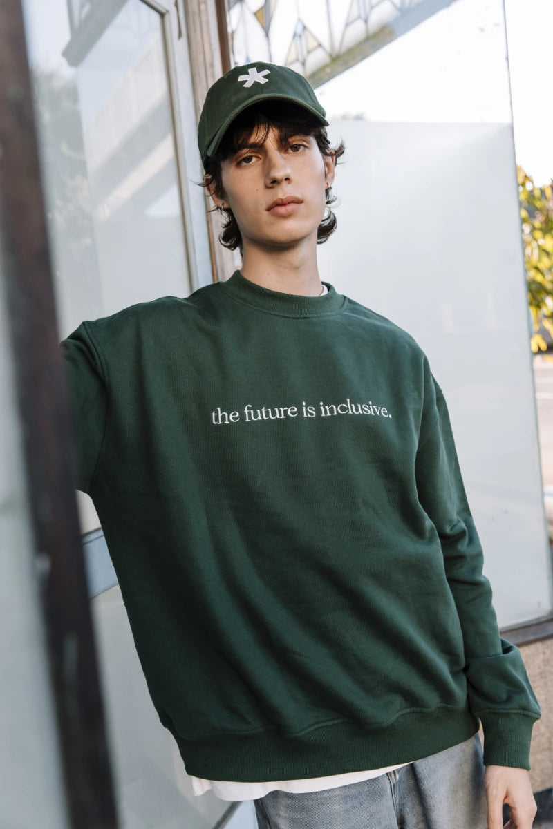 Person wearing a green sweatshirt with 'the future is inclusive' text, standing outdoors.